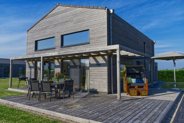A modern house with a wooden deck, a covered patio, and a barbecue area.