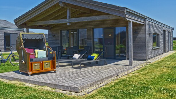 Ein modernes Gebäude mit einer überdachten Terrasse, ausgestattet mit Liegestühlen und einem Korbssessel-Sofa.
