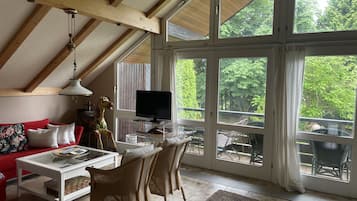 Un salon spacieux avec un haut plafond, de grandes fenêtres, un téléviseur et un coin salon confortable.
