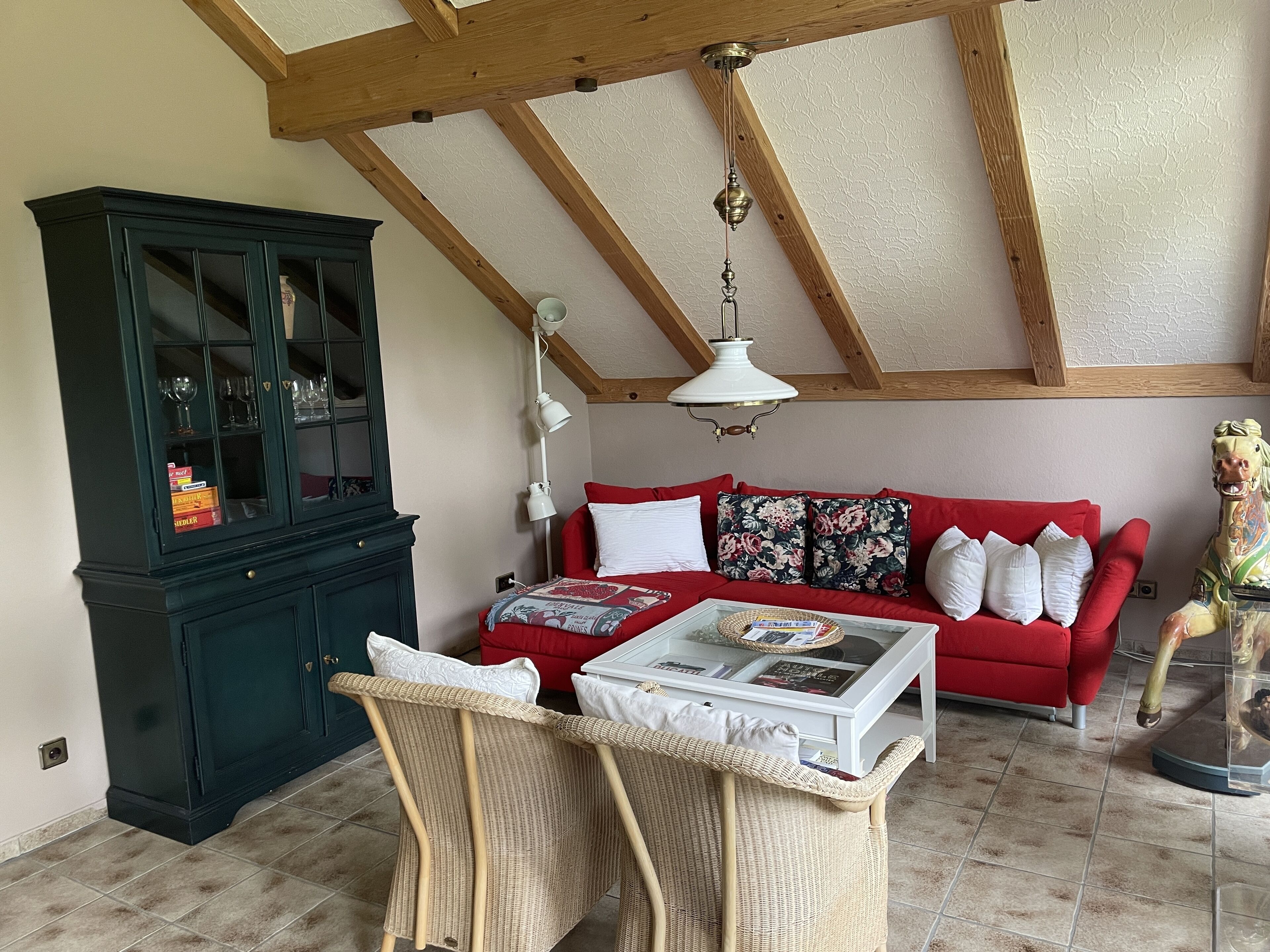 A living room with a red sofa, a glass coffee table, wicker chairs, a dark wooden cabinet, and a ceiling fan.