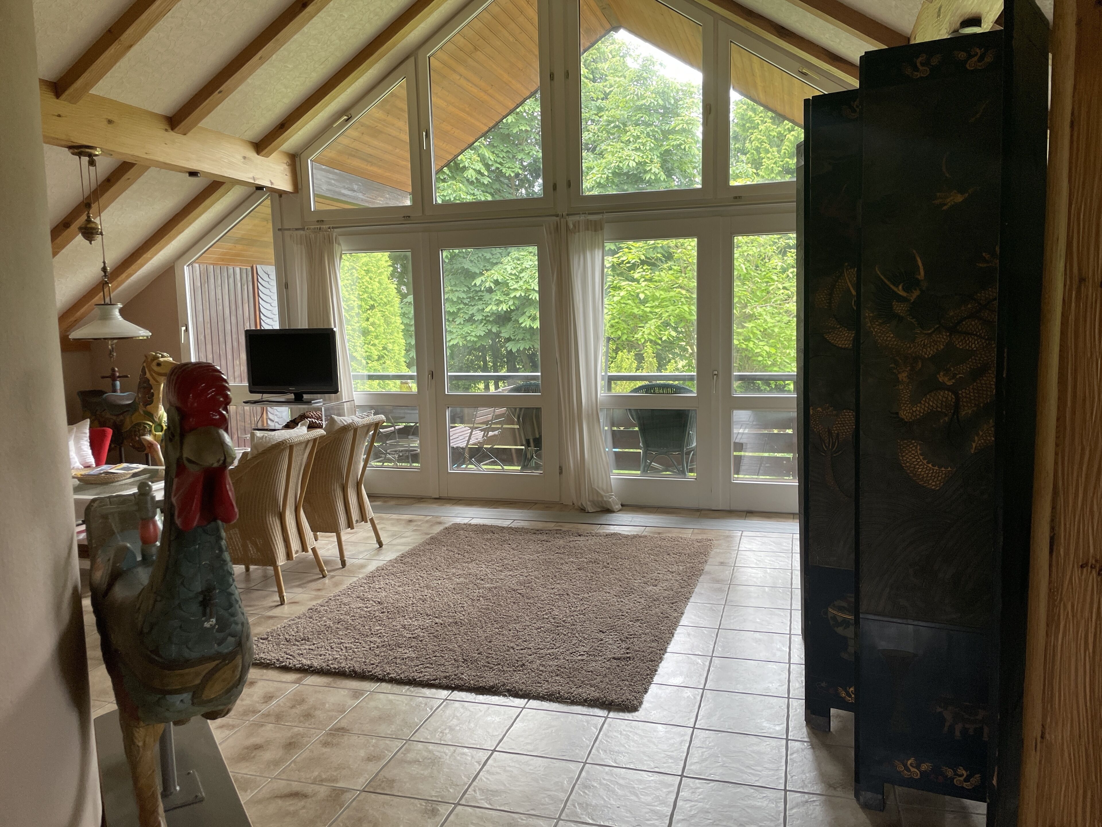 Ein geräumiger Raum mit hoher Decke, großen Fenstern, einem Fernseher und einer Essecke mit Stühlen und Tisch.