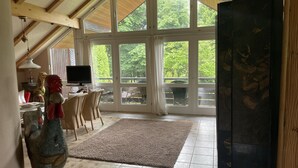 Ein geräumiger Raum mit hoher Decke, großen Fenstern, einem Fernseher und einer Essecke mit Stühlen und Tisch.