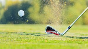 Ein Golfschläger trifft einen Ball auf dem Grün.
