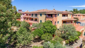 A multi-story residential building with balconies, surrounded by lush greenery. - Beach front apartment in Orosei (Orosei)