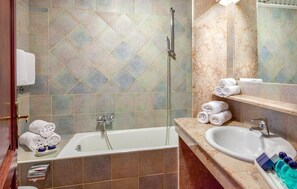 A bathroom with a bathtub, a sink, and a shower. There are towels and toiletries on the counter.
