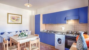 A compact kitchen with blue cabinets, a washing machine, and a dining area with a table and chairs. - Beach front apartment in Orosei (Orosei)