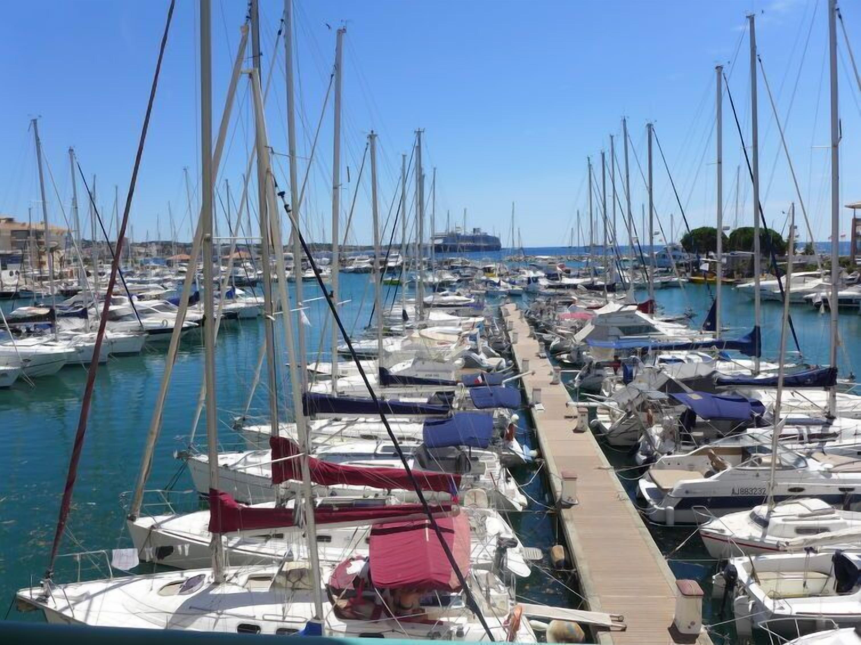 A marina with numerous sailboats docked in rows, connected by a wooden dock.