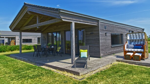 Een modern huis met een overdekte patio, buitenmeubels en een houten terras.