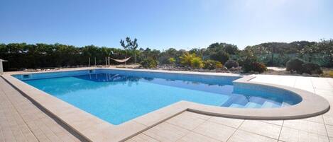 A rectangular swimming pool with a curved edge, surrounded by a tiled deck.