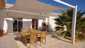 Eine Terrasse im Freien mit einem Holztisch und -stühlen, einem weißen Baldachin und einer Palme.