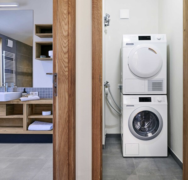 A modern bathroom with a built-in washer and dryer, wooden shelving, and a large mirror.