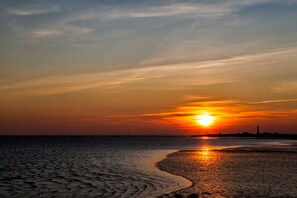 Un coucher de soleil sur une plage, avec un phare visible au loin.