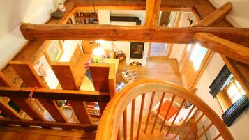 A wooden staircase with a view of a cozy room below, including a fireplace and a dining area.