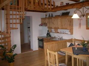 A wooden interior with a kitchen, dining area, staircase, and a small plant.