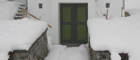 Una entrada cubierta de nieve con un muro de piedra, una escalera de madera y una puerta verde.