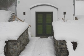 Una entrada cubierta de nieve con un muro de piedra, una escalera de madera y una puerta verde.