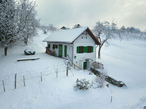 A snow-covered house with a sloped roof, green shutters, and a visible year '1952' on the facade.
