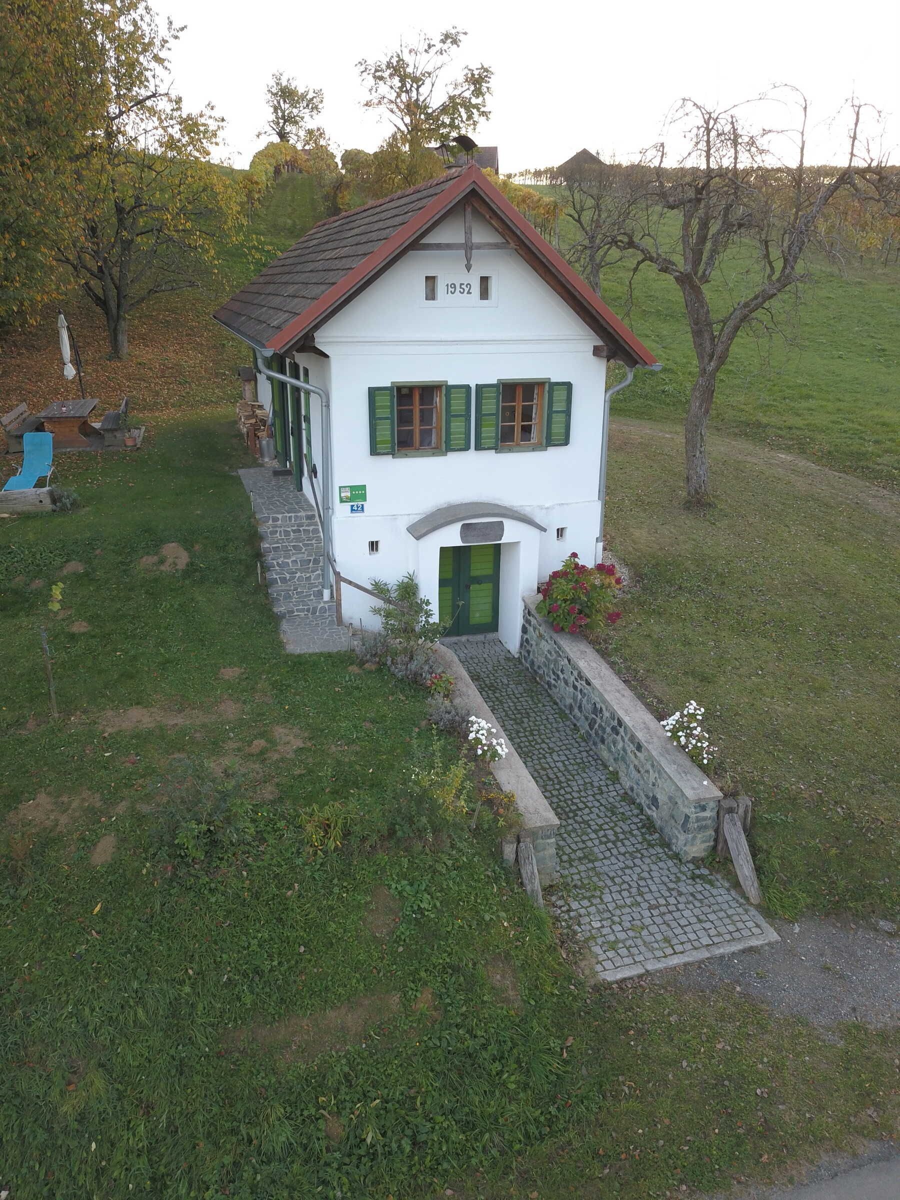 Un bâtiment blanc avec des volets verts, un escalier en pierre et le numéro « 19 52 » inscrit sur le toit.