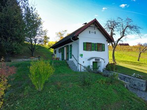 A white building with green shutters, a stone staircase, and a stone wall.
