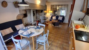 Un comedor acogedor con una mesa redonda, sillas y un sofá. Se ve una cocina con un fregadero y una estufa al fondo.
