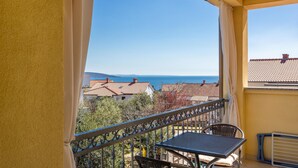 Un balcón con mesa y sillas, con vistas a la costa, casas y el mar.