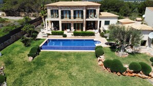 A two-story stone house with a swimming pool, surrounded by well-maintained lawns and trees.