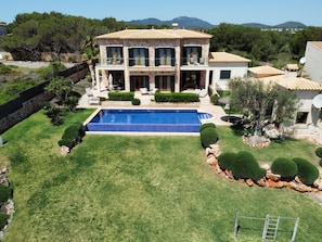 Uma casa de pedra de dois andares com piscina, cercada por jardins e árvores bem cuidadas.