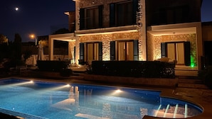 A modern two-story house with a swimming pool, stone facade, and green shutters.