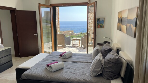 A bedroom with a bed, a view of the sea, and a balcony with outdoor furniture.