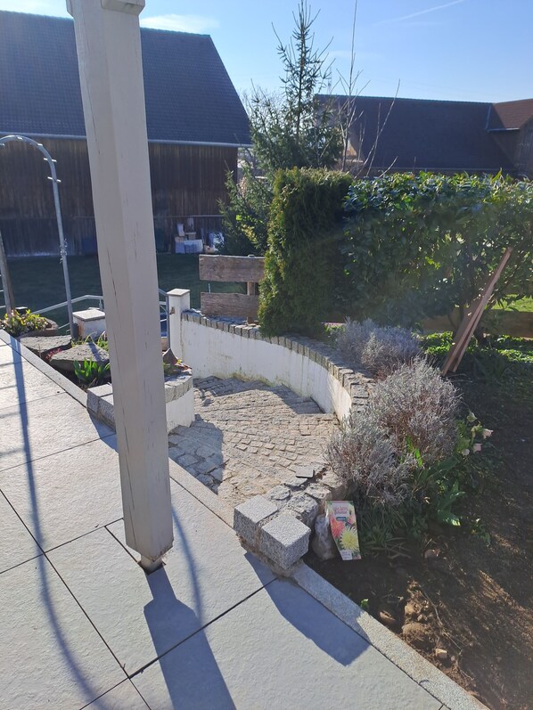 Un patio empedrado con un muro de piedra, un banco de madera y un jardín con diversas plantas.
