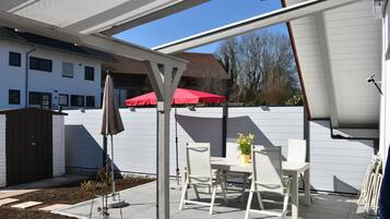 Eine Terrasse mit Tisch und Stühlen, einem roten Sonnenschirm und einem weißen Zaun.