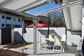 Un patio con una mesa, sillas, un paraguas rojo y una cerca blanca.