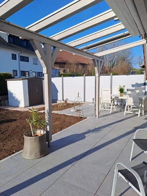 Un área de patio techada con una pérgola, mobiliario exterior y un pequeño jardín.