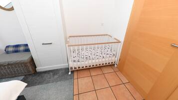Ein Zimmer mit einem weißen Babybett, einer Holztür und einem grauen Teppich.