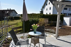 Un patio con una mesa redonda, dos sillas, un florero con flores y una estructura de pérgola.