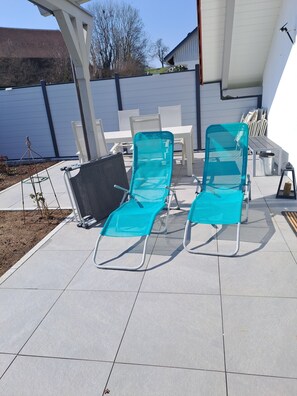 Un patio al aire libre con dos sillones turquesa, una mesa blanca y una silla metálica.