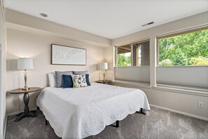 A bedroom with a large bed, two bedside tables, a wall-mounted lamp, and a window with blinds. - Shore View Home Retreat (Manson)