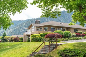 A two-story house with a balcony, surrounded by well-maintained gardens and a view of a forested mountain range. - Shore View Home Retreat (Manson)