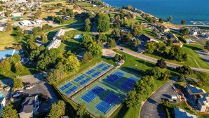 Una vista aerea di una zona residenziale con case, un complesso di campi da tennis e un lago sullo sfondo.