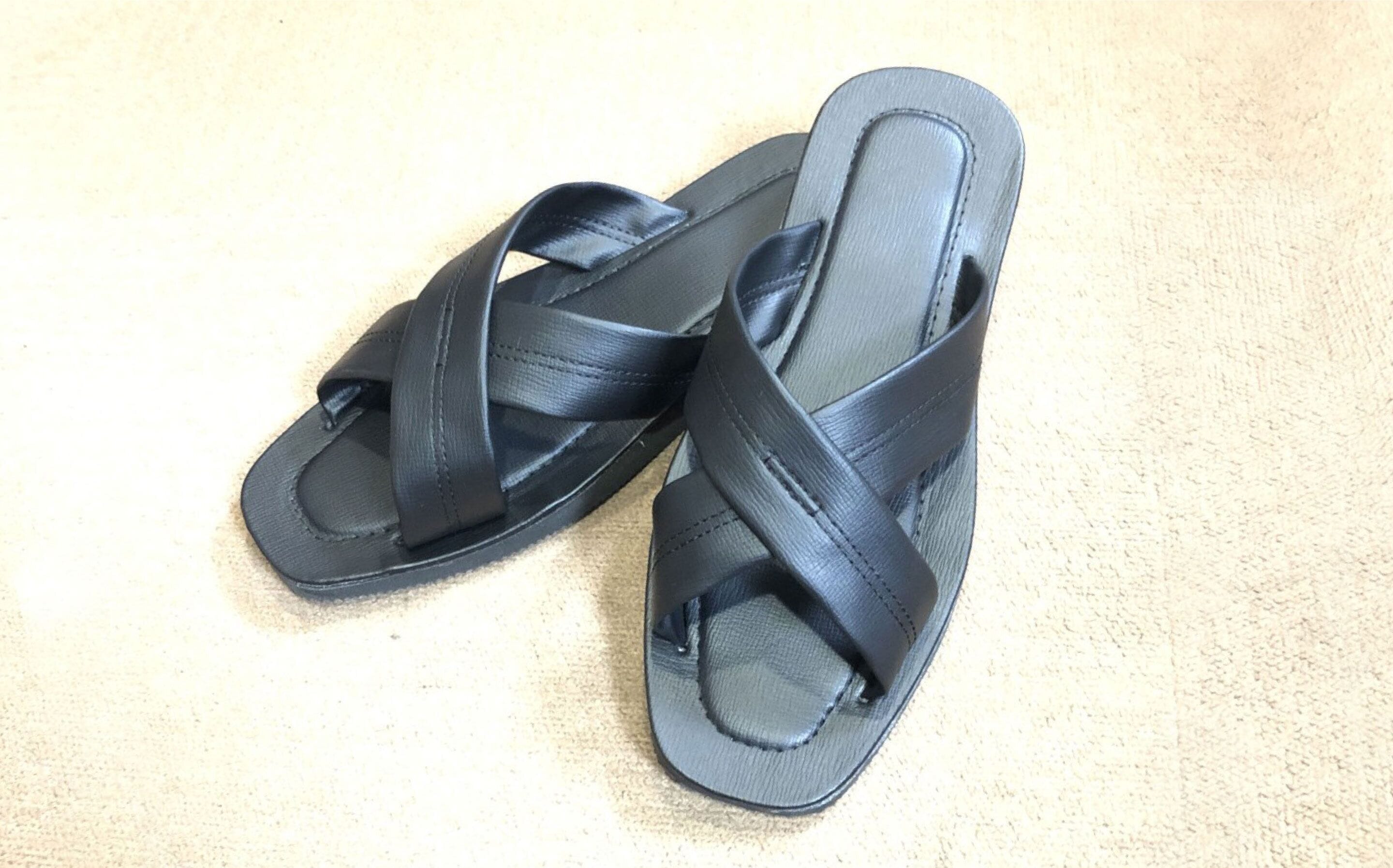 A pair of black sandals with a strap design, placed on a textured surface.