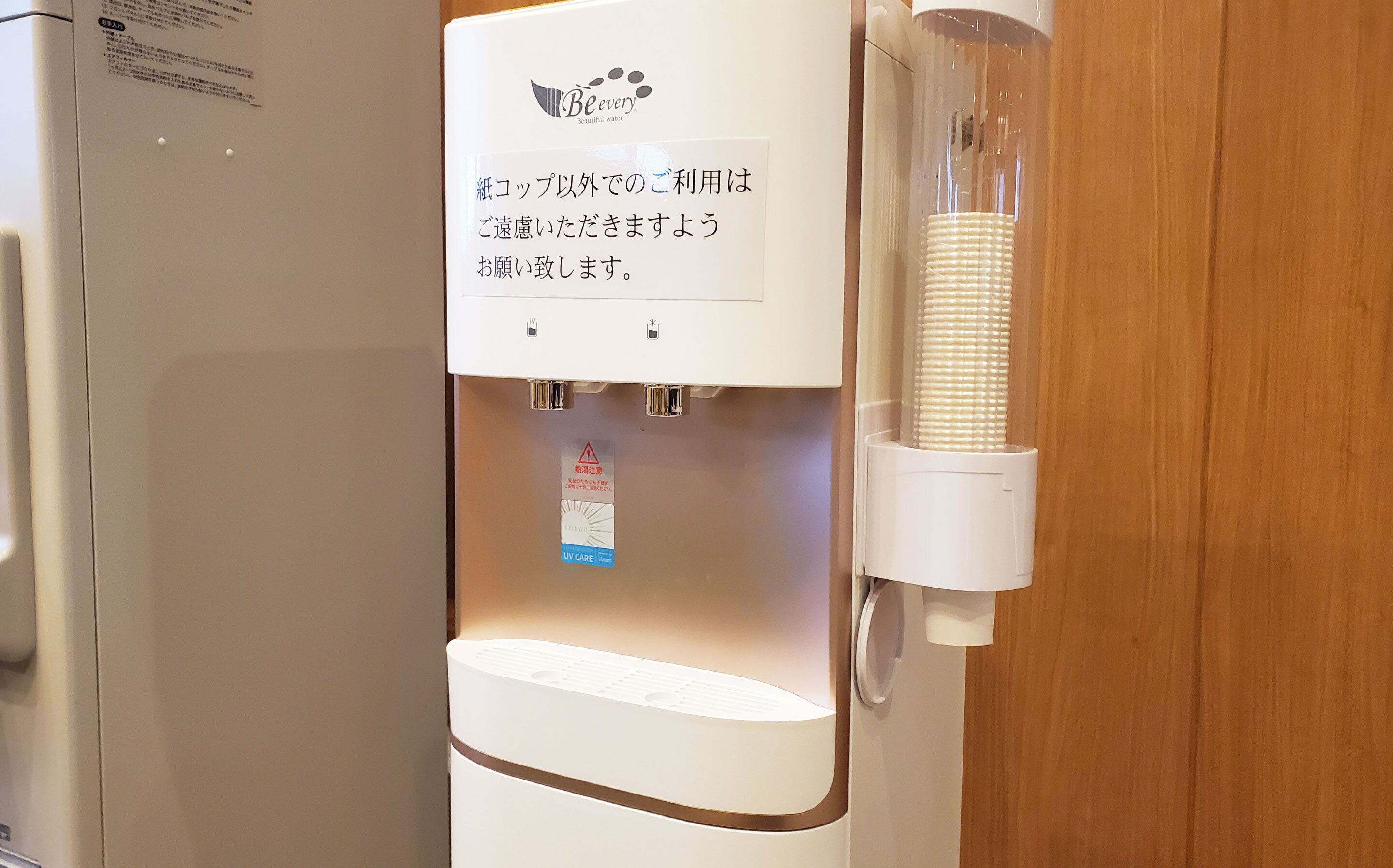 A water dispenser with a sign in Japanese, a UV indicator, and a paper towel dispenser.