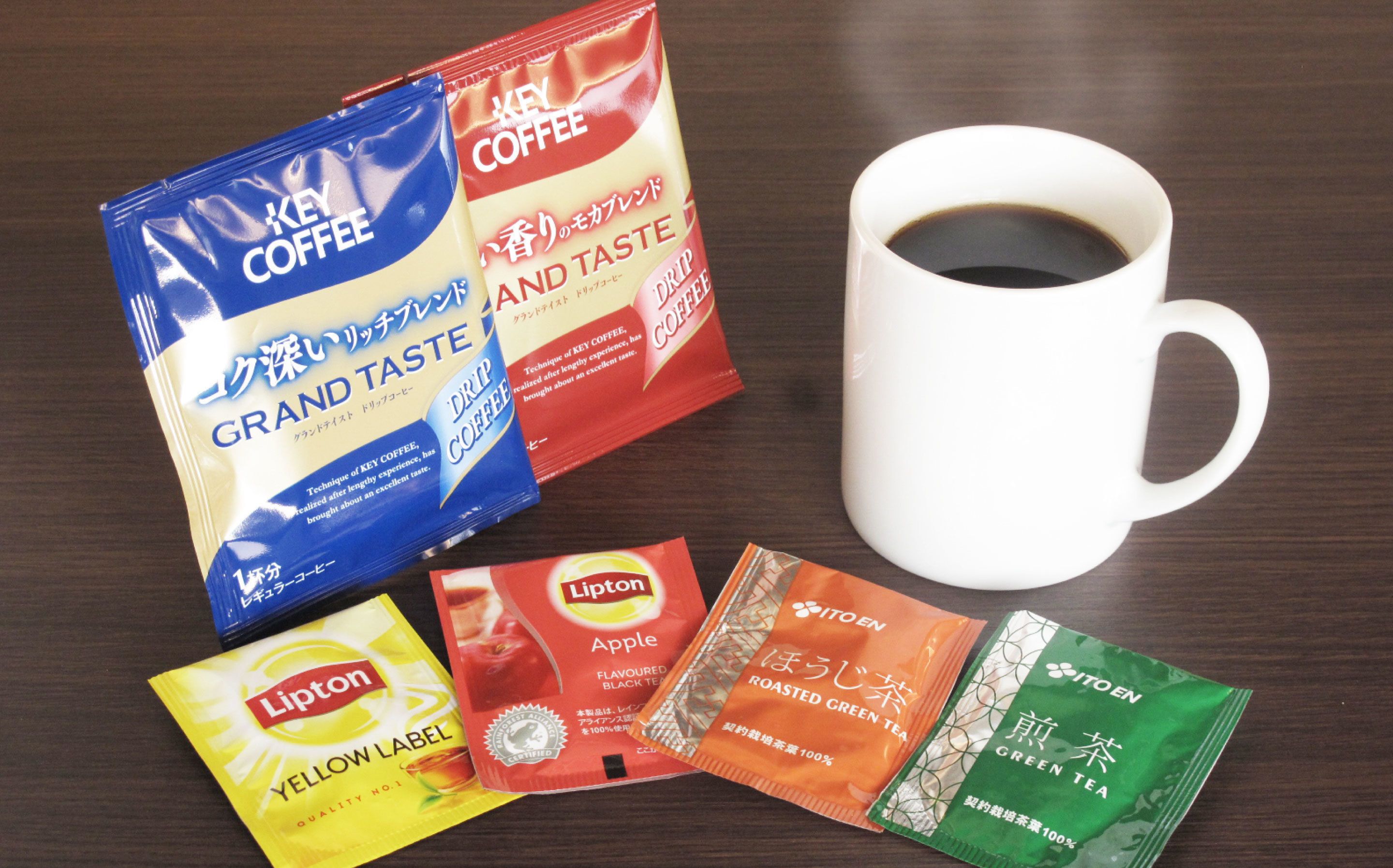 Une tasse à café blanche et divers sachets de café et de thé sont posés sur une surface en bois.