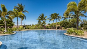 Piscina azul cristalina rodeada de palmeras y follaje, con cielo despejado.