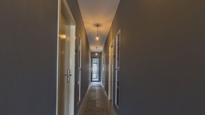 A long, narrow hallway with patterned floor tiles, white-framed doors, and a ceiling light fixture.