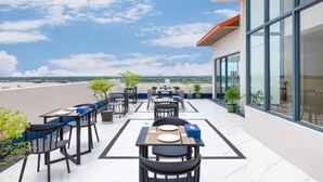 A rooftop terrace with tables and chairs, potted plants, and a view of the beach. - Hotel Balmi (Yangon)