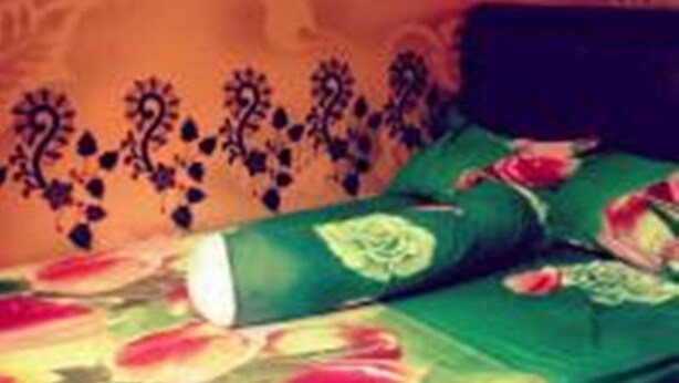 Un lit avec une literie verte et un motif floral, une tête de lit sombre et un mur orné d’une bordure décorative.