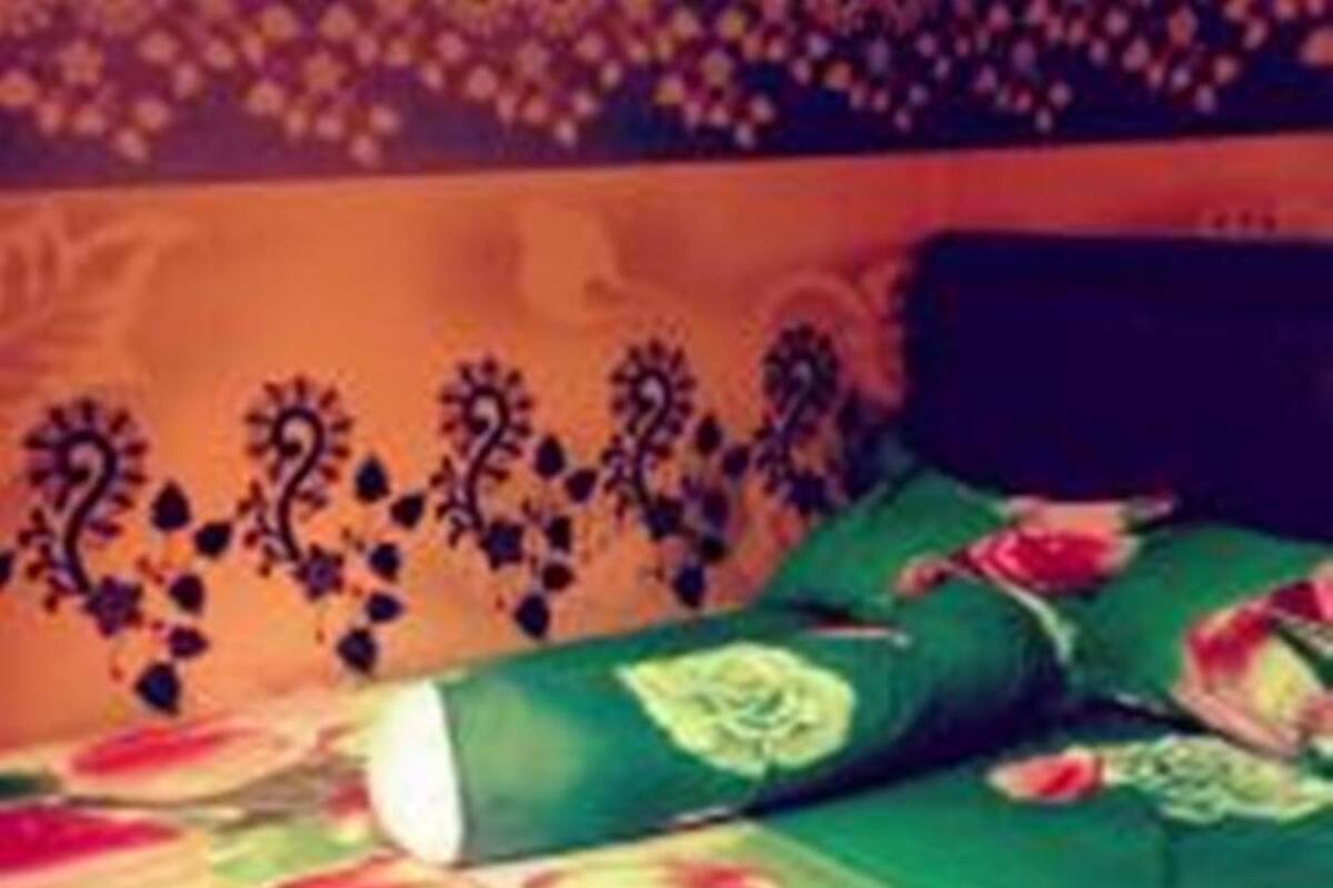 A bed with green bedding and a floral pattern, a dark headboard, and a wall with a decorative border.