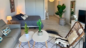 A modern hotel room with a bed, a sofa, a chair, a small table, and a large plant. - Lagoon front Magnificent Studio completely renovated with panoramic lagoon view (Saint-Martin)