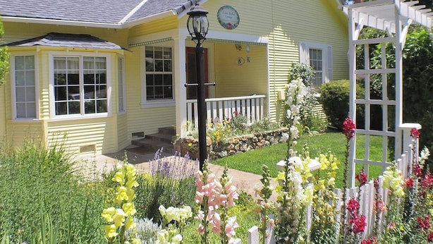 Una casa gialla con veranda e giardino ricco di fiori.