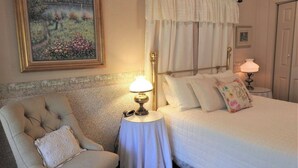 Una camera da letto con un letto, una sedia, un comodino con una lampada e un quadro appeso al muro.
